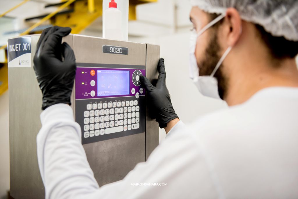 Profissional da indústria cosmética operando maquinário automatizado em ambiente esterilizado, representando eficiência e tecnologia na terceirização de produção.